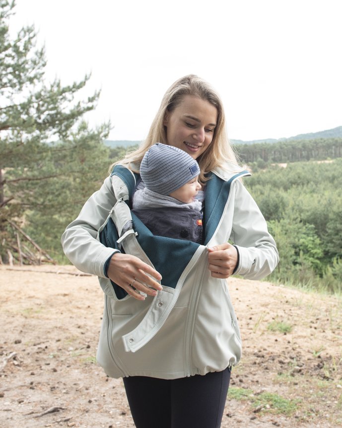 Mom zipping the baby insert of her light mamalila softshell babywearing jacket over her baby in the carrier, outdoors