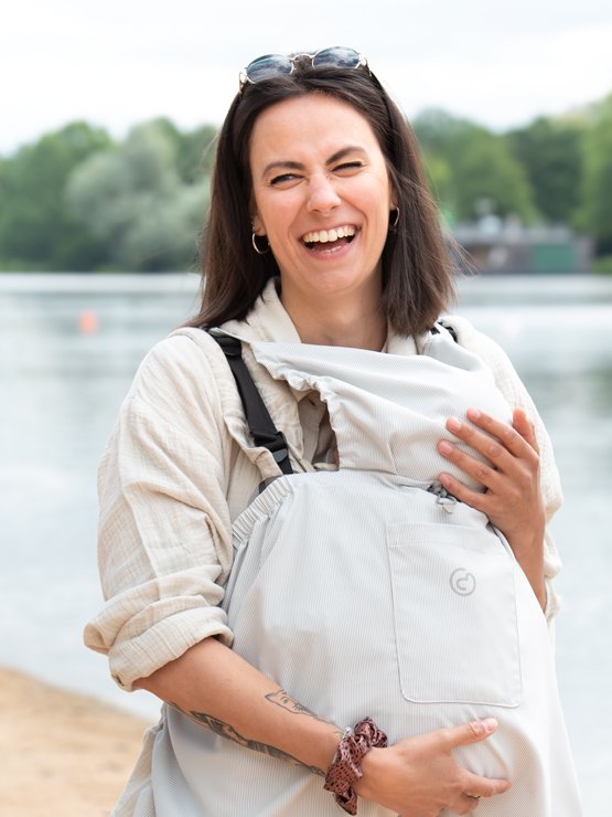 Laughing mom by the lake carrying her baby under the light mamalila UV cover