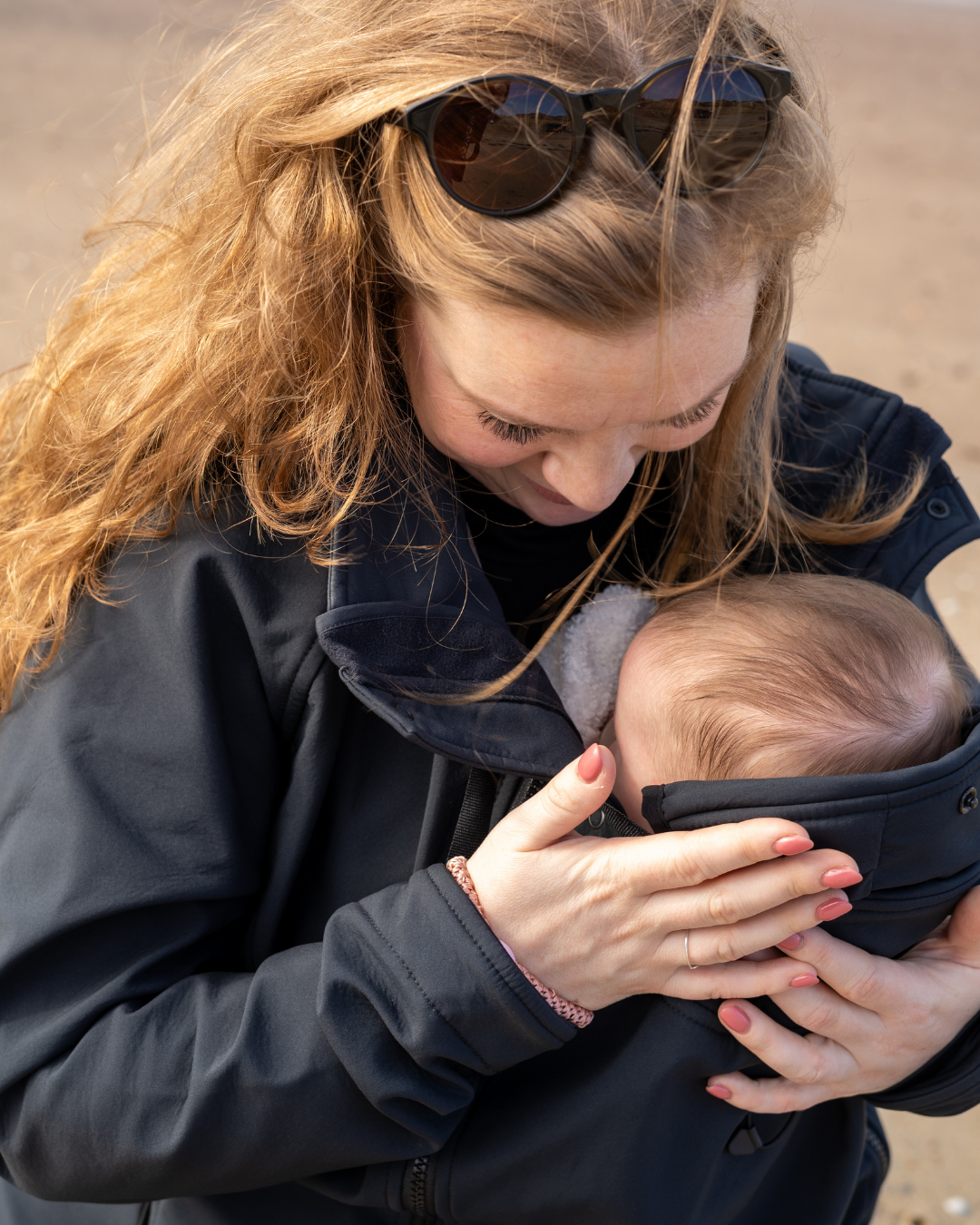 Frau trägt Baby nah am Körper in dunkler Tragejacke im Freien