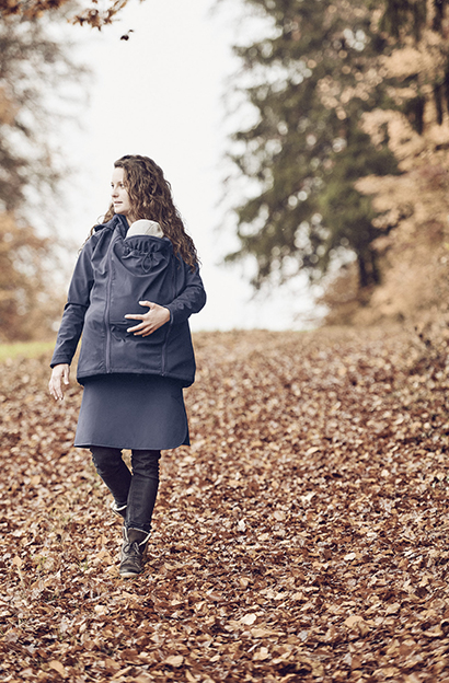 Mutter geht mit Kind in derTragejacke im Herbstlaub spazieren