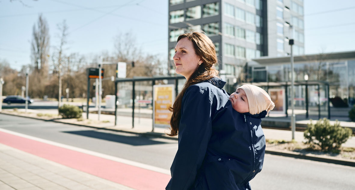 Mother carries child on her back under coat