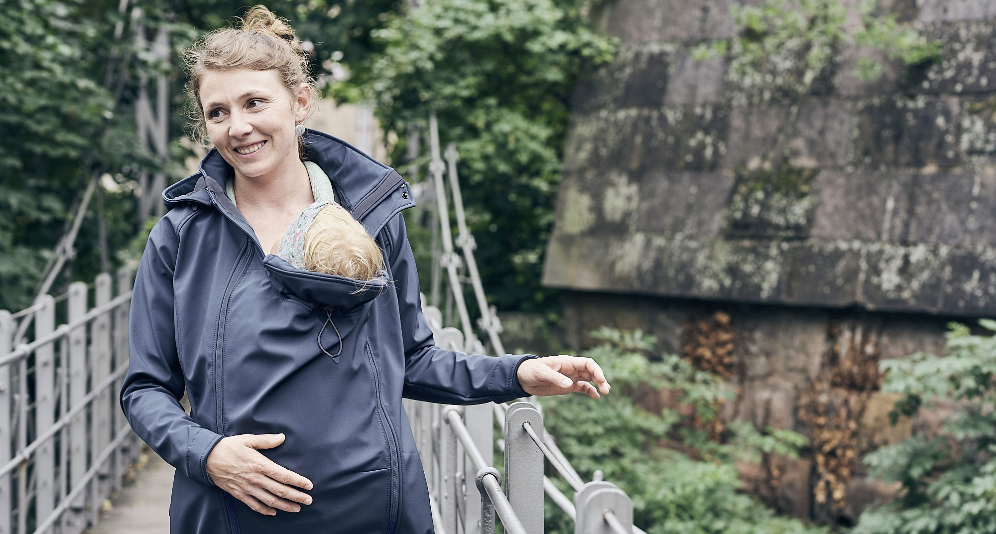 Mother crossing bridge with child under jacket