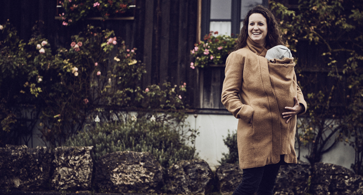 Woman carries her baby under the wool coat