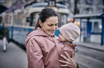 Mutter mit Kind in der Trage vor einer Straßenbahn