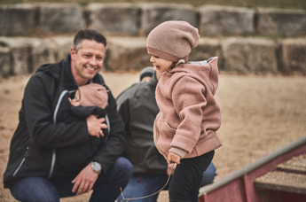 Papa mit Tragebaby ist auf dem Spielplatz mit der großen Schwester
