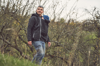 Papa mit Kind in der Jacke steht an einem Hang