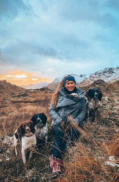 Outdoor mom sitting with child under jacket and 3 dogs in a field in Norway
