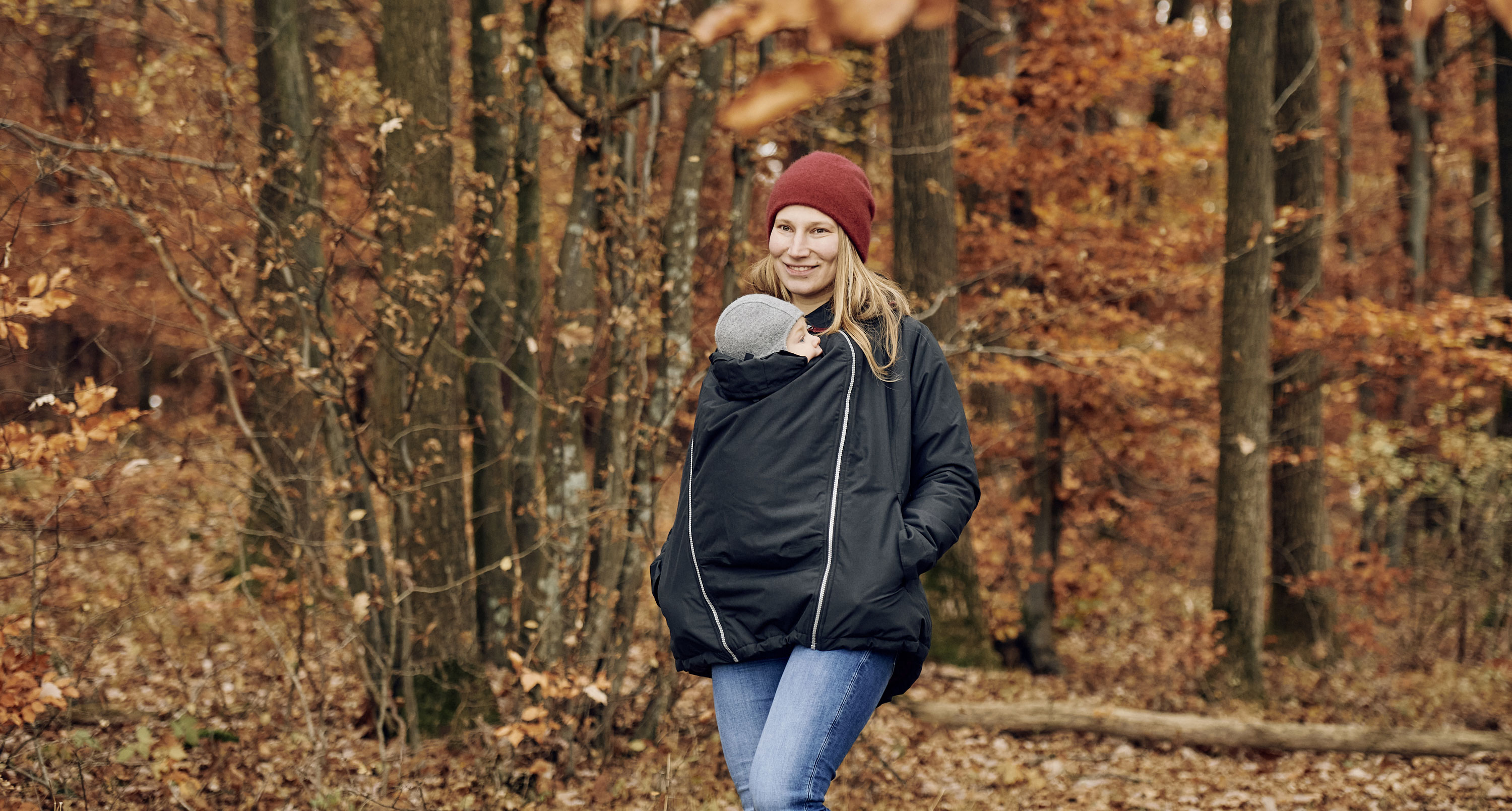 Mutter geht mit Kind unter der Jacke im Herbstwald spazieren