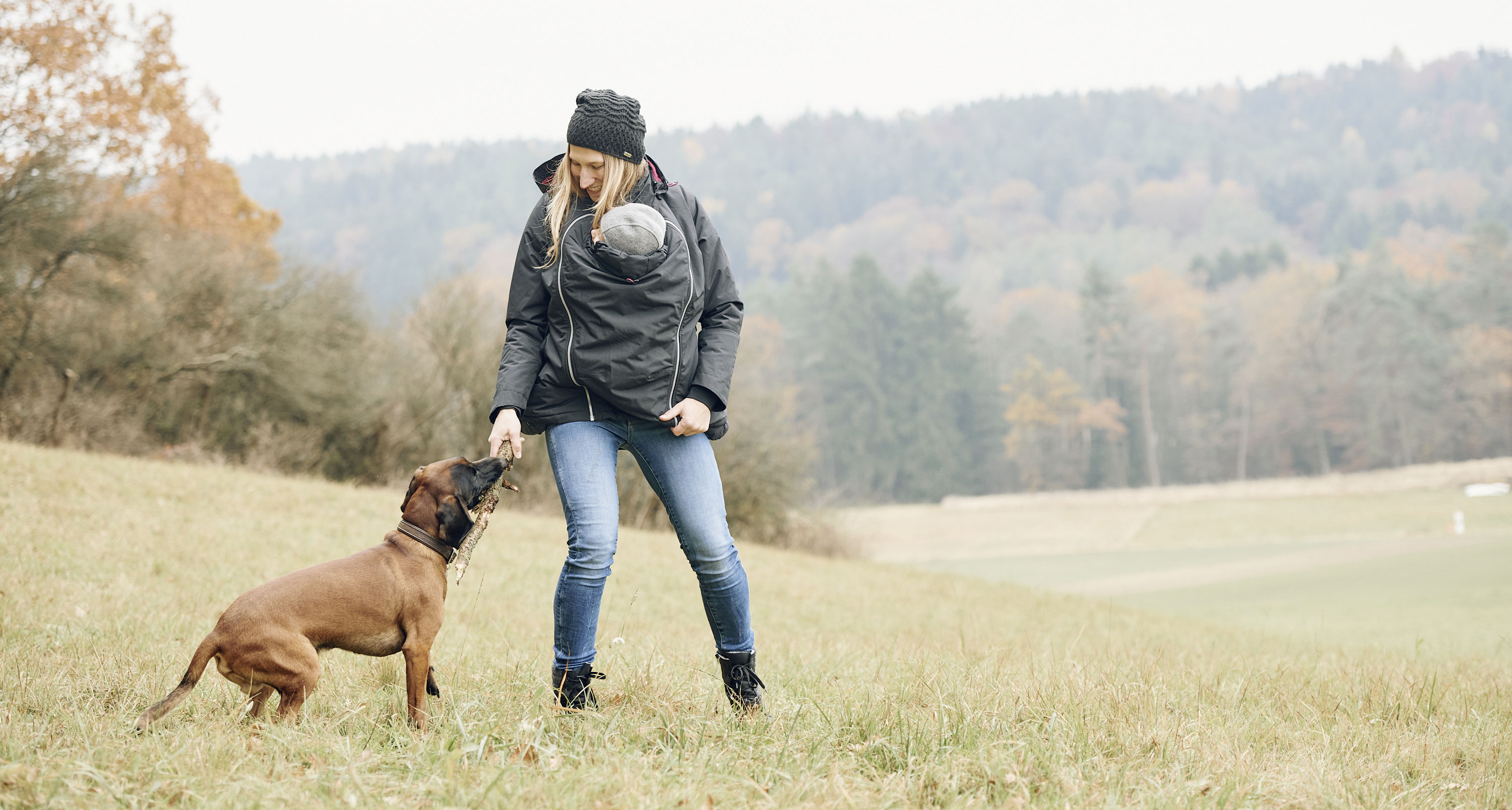 om with child under jacket playing with dog on meadow