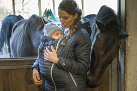 Mutter und Baby mit Wintersteppjacke im Pferdestall