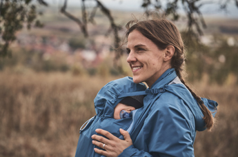 Mutter und Baby mit Regentragejacke im Herbst auf einer Wiese