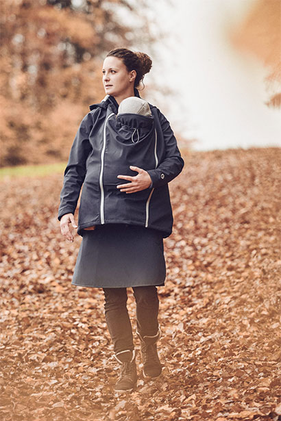 Mutter geht mit Kind in derTragejacke im Herbstlaub spazieren